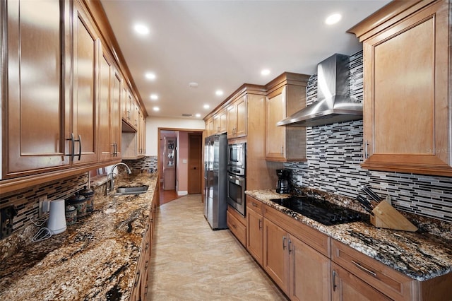 kitchen featuring dark stone counters, sink, stainless steel appliances, and wall chimney range hood