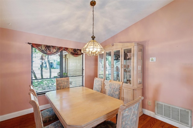 dining area featuring hardwood / wood-style floors, an inviting chandelier, and vaulted ceiling