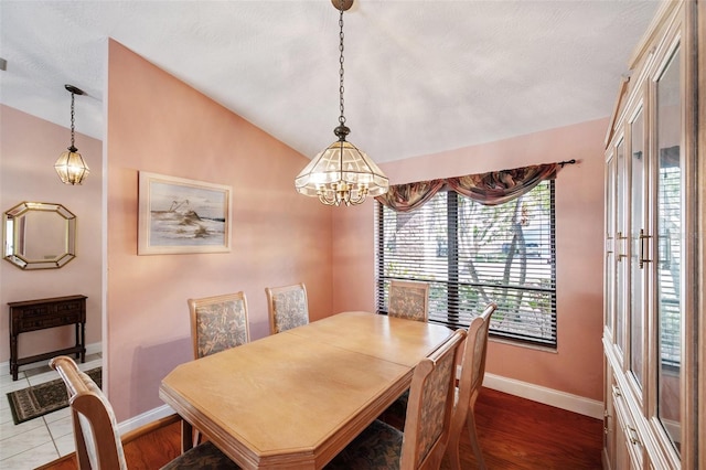 dining room featuring wood-type flooring, a textured ceiling, vaulted ceiling, and a notable chandelier