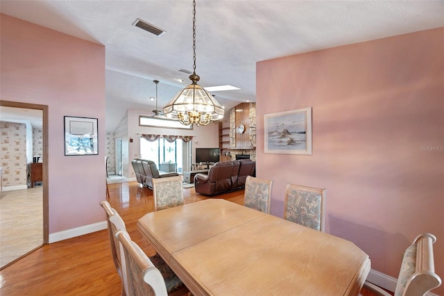 dining area with a chandelier, vaulted ceiling, a textured ceiling, and light hardwood / wood-style flooring