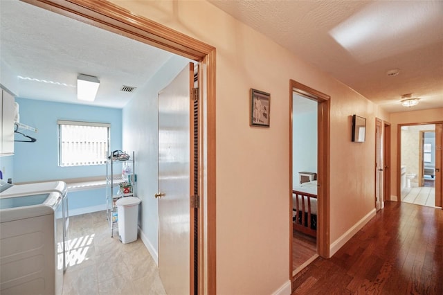 corridor with hardwood / wood-style flooring, washing machine and dryer, and a textured ceiling