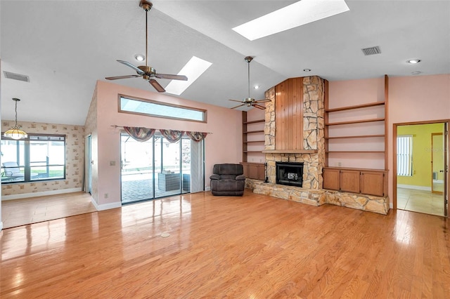 unfurnished living room with ceiling fan, a fireplace, a skylight, and light hardwood / wood-style floors