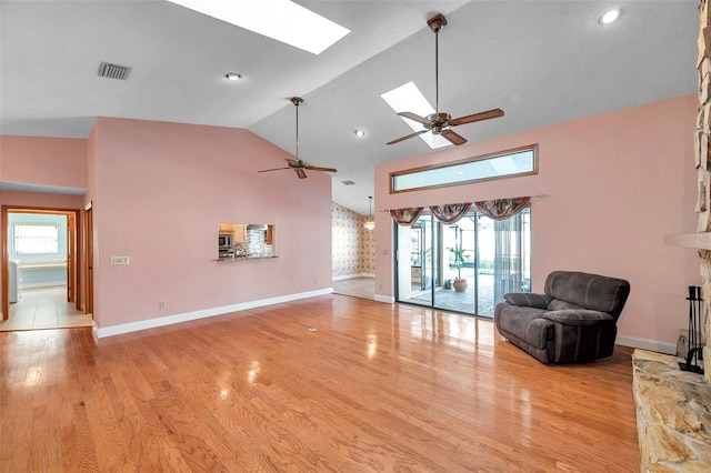 unfurnished living room with ceiling fan, a stone fireplace, light hardwood / wood-style flooring, and vaulted ceiling with skylight