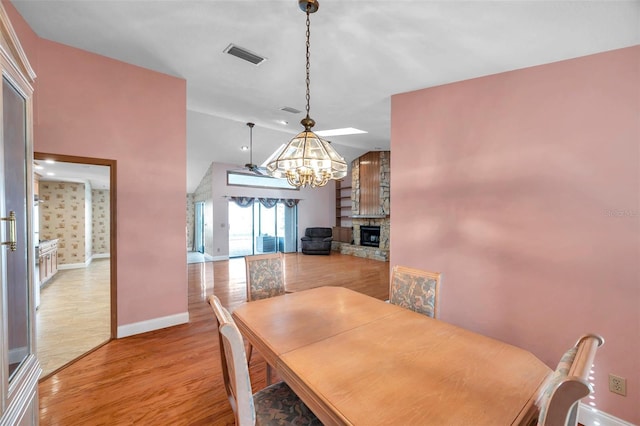 dining area featuring a fireplace, vaulted ceiling, a chandelier, and light wood-type flooring