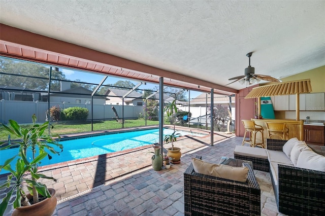 view of pool with an outdoor bar, ceiling fan, glass enclosure, a patio area, and an outdoor hangout area