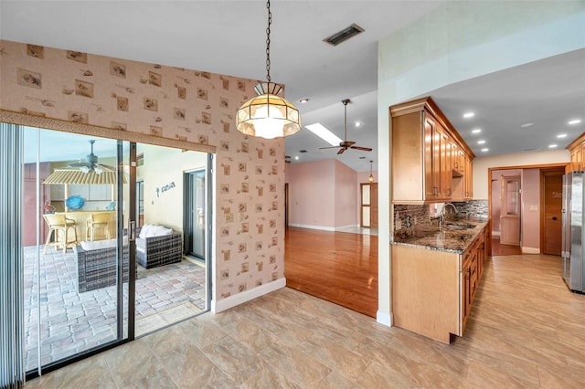 kitchen featuring sink, hanging light fixtures, dark stone countertops, stainless steel refrigerator, and ceiling fan