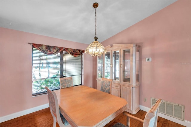 dining space with wood-type flooring, vaulted ceiling, and a notable chandelier