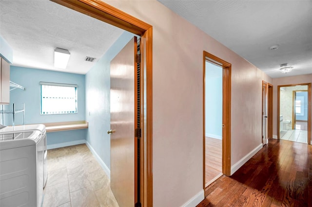 hall with hardwood / wood-style floors, independent washer and dryer, a wealth of natural light, and a textured ceiling