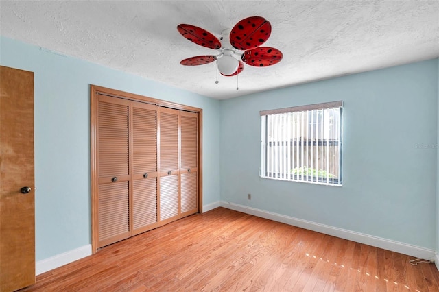 unfurnished bedroom featuring ceiling fan, a closet, light hardwood / wood-style flooring, and a textured ceiling