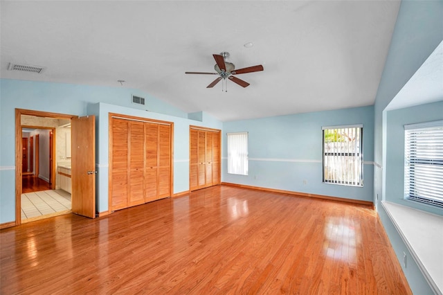 unfurnished bedroom with light hardwood / wood-style flooring, ceiling fan, connected bathroom, vaulted ceiling, and multiple closets