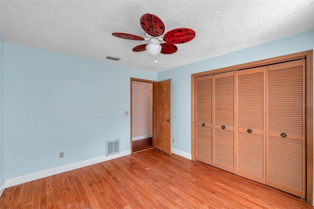 unfurnished bedroom with ceiling fan, a textured ceiling, light hardwood / wood-style floors, and a closet