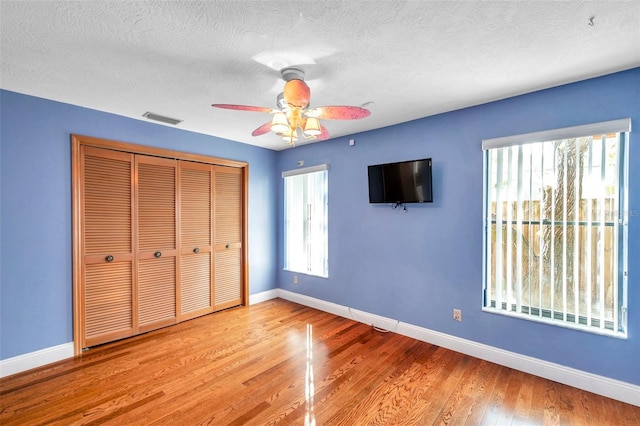 unfurnished bedroom featuring multiple windows, a textured ceiling, light hardwood / wood-style floors, and a closet