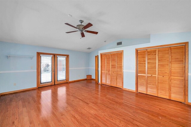 unfurnished bedroom featuring lofted ceiling, two closets, light hardwood / wood-style flooring, and ceiling fan