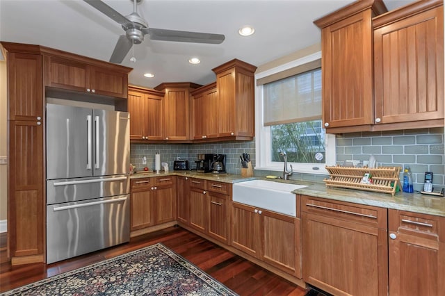 kitchen with dark wood-type flooring, sink, light stone counters, and stainless steel refrigerator