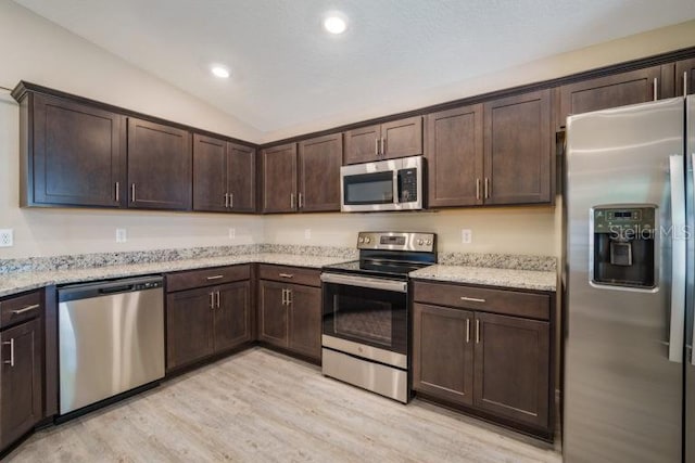 kitchen featuring dark brown cabinetry, appliances with stainless steel finishes, lofted ceiling, and light stone counters