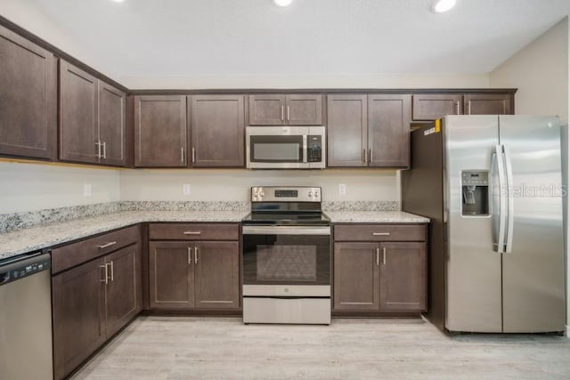 kitchen with dark brown cabinetry, light stone countertops, stainless steel appliances, and light hardwood / wood-style flooring