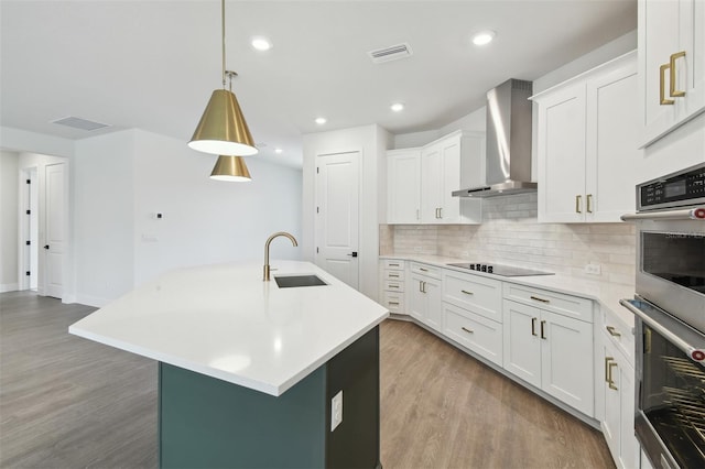 kitchen featuring decorative light fixtures, white cabinetry, sink, a kitchen island with sink, and wall chimney range hood