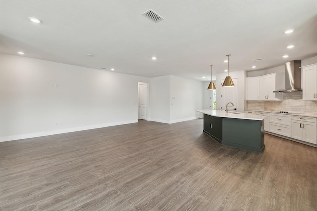 kitchen with sink, white cabinets, hanging light fixtures, a center island with sink, and wall chimney exhaust hood