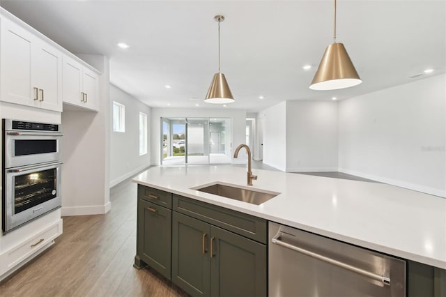 kitchen featuring appliances with stainless steel finishes, hardwood / wood-style floors, sink, white cabinets, and hanging light fixtures