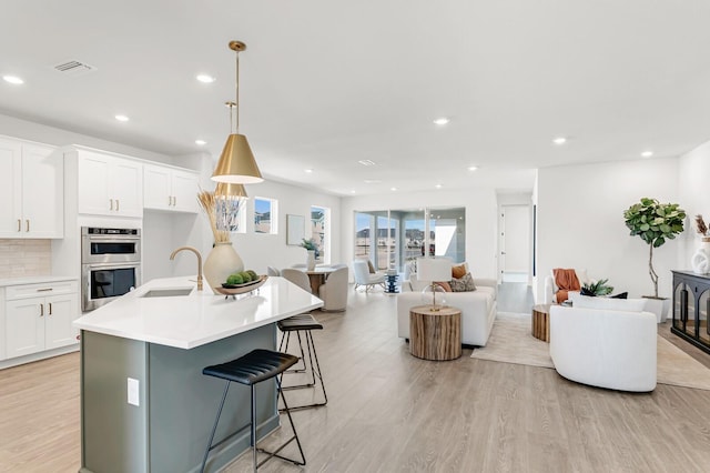 kitchen with stainless steel double oven, a sink, open floor plan, light wood-style floors, and recessed lighting