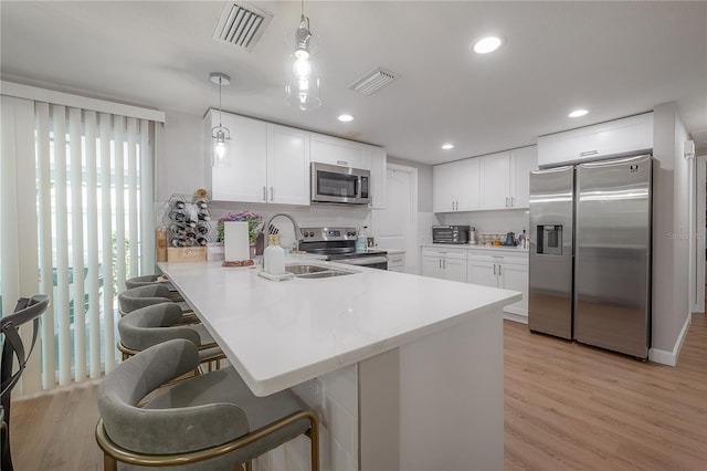 kitchen with white cabinets, kitchen peninsula, appliances with stainless steel finishes, and pendant lighting