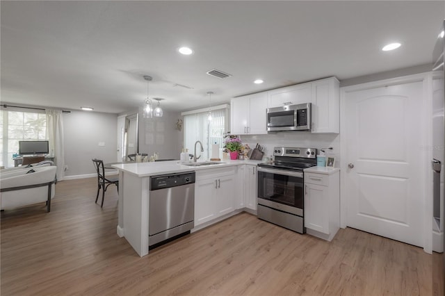 kitchen featuring white cabinetry, sink, kitchen peninsula, appliances with stainless steel finishes, and hanging light fixtures