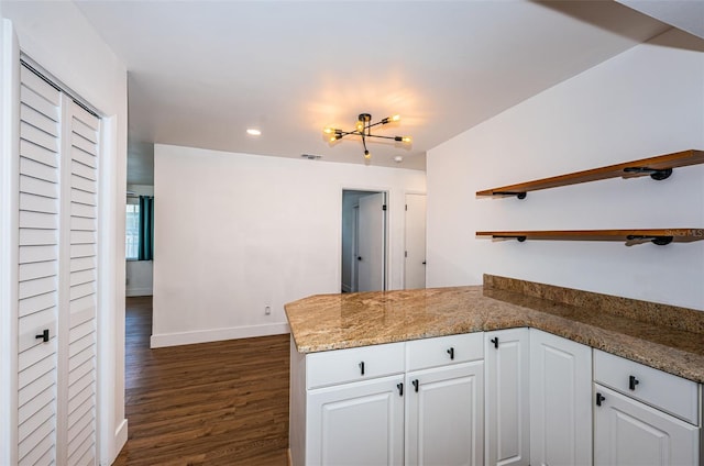 kitchen featuring dark wood-type flooring, white cabinets, kitchen peninsula, a chandelier, and stone countertops