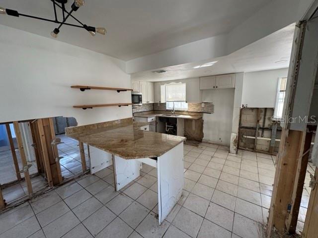 kitchen featuring light tile patterned flooring, white cabinetry, a kitchen bar, sink, and kitchen peninsula