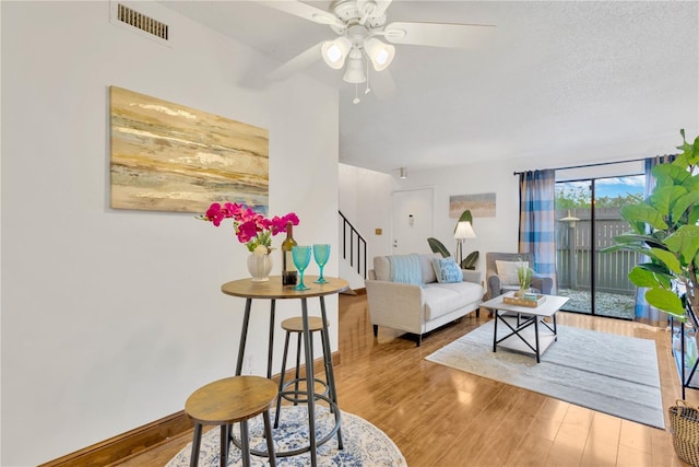 living room with ceiling fan, light wood-type flooring, and a textured ceiling