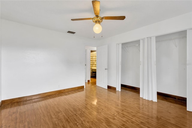 unfurnished bedroom with hardwood / wood-style floors, ceiling fan, and multiple closets