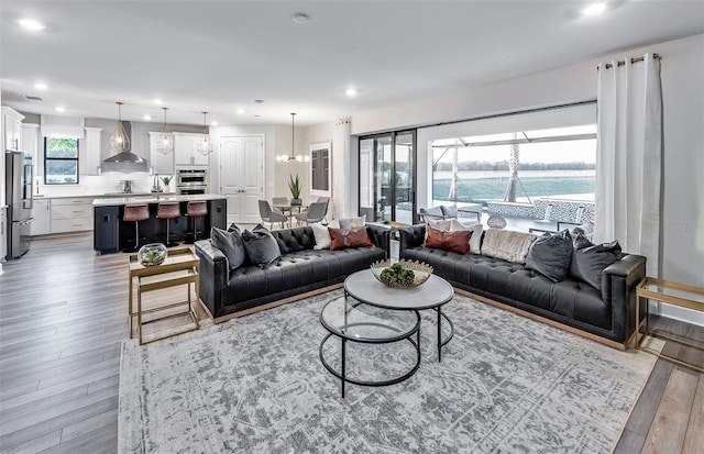 living room featuring an inviting chandelier, sink, a water view, and light hardwood / wood-style flooring