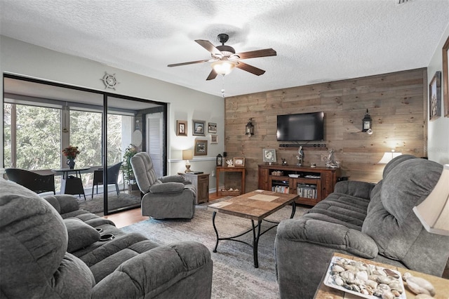 living room with wood walls, ceiling fan, a textured ceiling, and light hardwood / wood-style floors