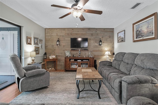 living room with a textured ceiling, wooden walls, hardwood / wood-style flooring, and ceiling fan