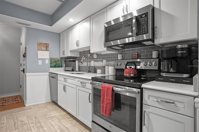 kitchen with light parquet flooring, stainless steel appliances, white cabinetry, decorative backsplash, and sink