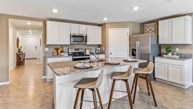 kitchen featuring light stone countertops, white cabinets, a center island with sink, and stainless steel appliances