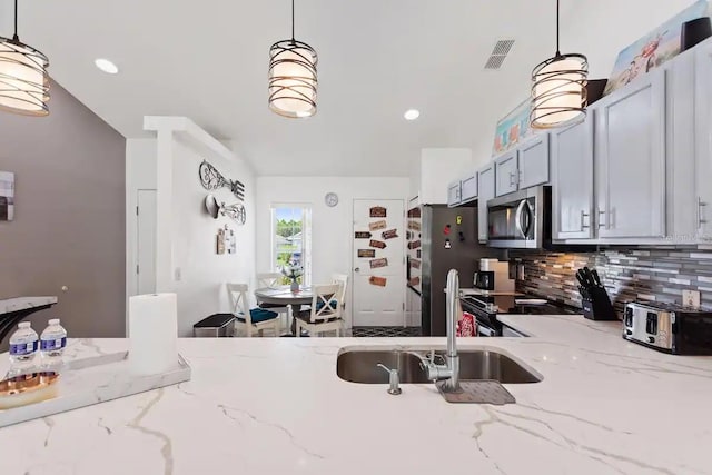 kitchen featuring light stone countertops, appliances with stainless steel finishes, hanging light fixtures, and sink