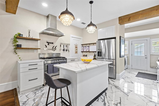 kitchen with light stone countertops, white cabinetry, stainless steel appliances, wall chimney range hood, and a kitchen island