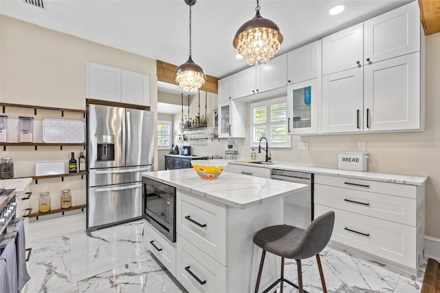 kitchen featuring light stone countertops, appliances with stainless steel finishes, decorative light fixtures, white cabinets, and a center island