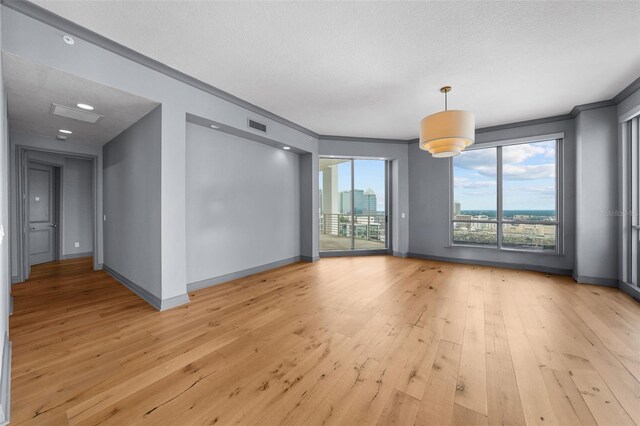 empty room with a textured ceiling, light wood-type flooring, and crown molding