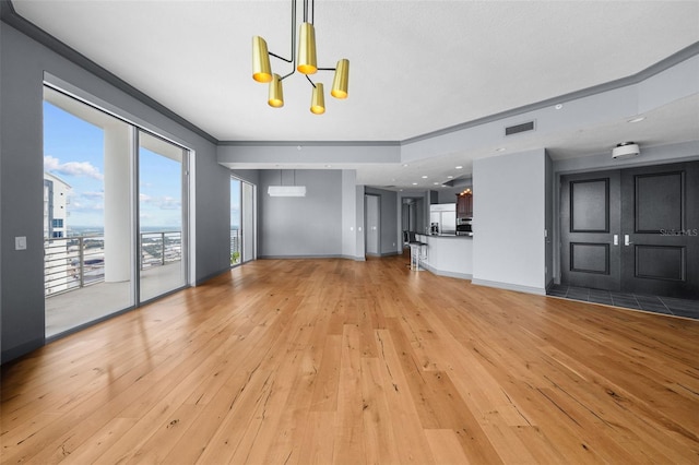 unfurnished living room featuring ornamental molding, a chandelier, and light hardwood / wood-style floors