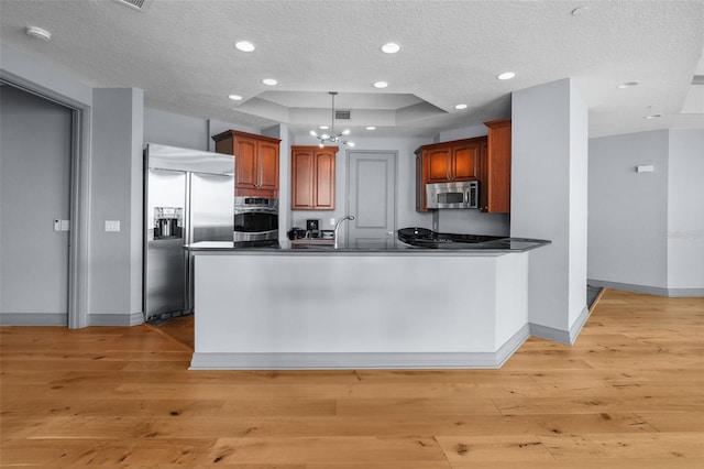 kitchen with kitchen peninsula, appliances with stainless steel finishes, a textured ceiling, a tray ceiling, and light hardwood / wood-style flooring