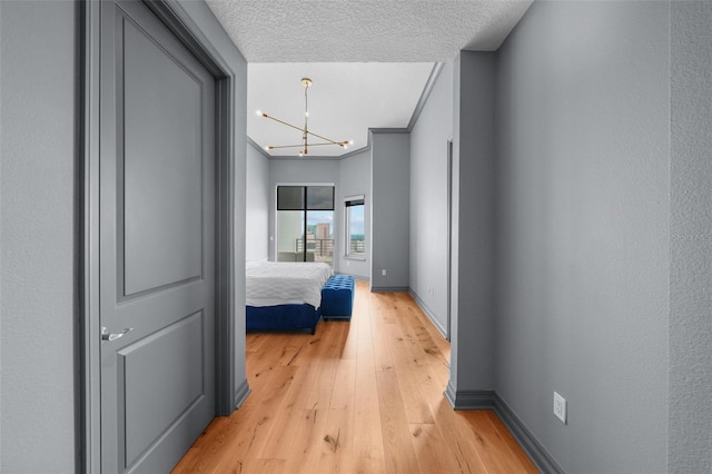 corridor featuring ornamental molding, light hardwood / wood-style floors, a textured ceiling, and a chandelier