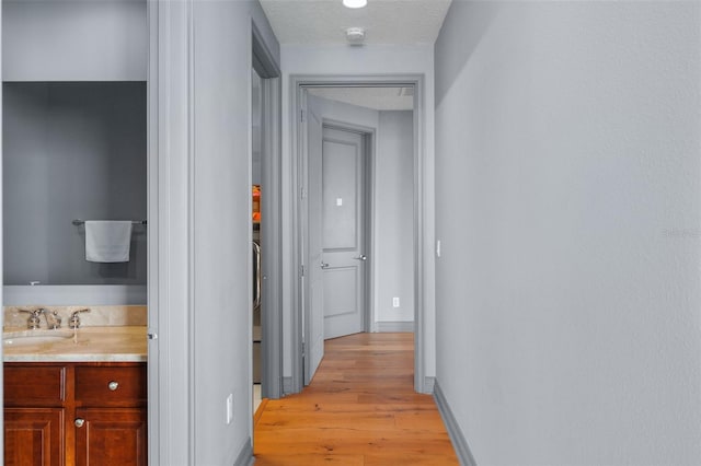 hallway featuring a textured ceiling, light hardwood / wood-style flooring, and sink