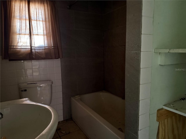 bathroom with tile patterned flooring, a bath, toilet, and tile walls