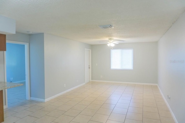 empty room featuring a textured ceiling, a ceiling fan, light tile patterned floors, and baseboards
