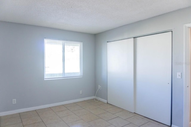unfurnished bedroom with a textured ceiling, a closet, baseboards, and light tile patterned flooring