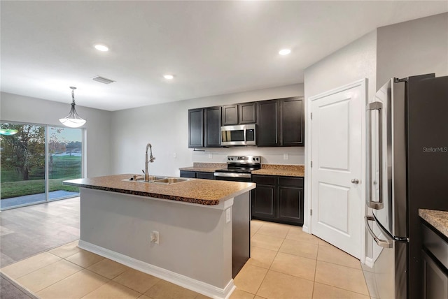 kitchen featuring a center island with sink, sink, light tile patterned floors, pendant lighting, and appliances with stainless steel finishes