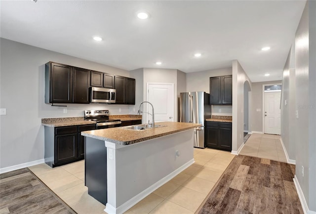 kitchen with stainless steel appliances, dark brown cabinets, light hardwood / wood-style flooring, sink, and a kitchen island with sink