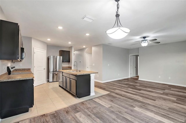 kitchen featuring stainless steel appliances, light wood-type flooring, decorative light fixtures, sink, and an island with sink