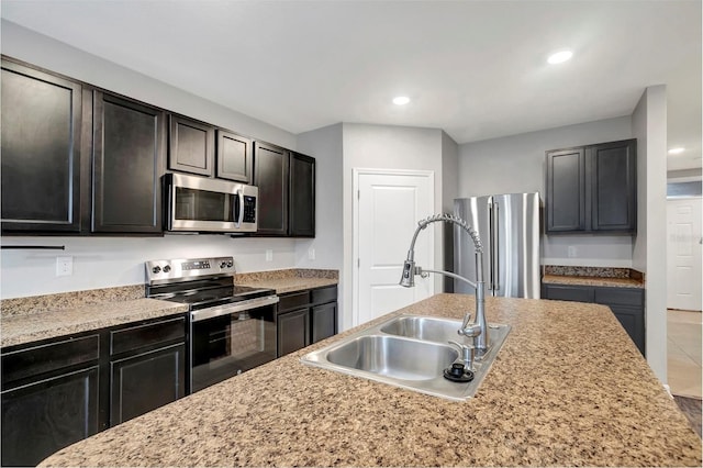 kitchen with a kitchen island with sink, stainless steel appliances, sink, and light stone counters